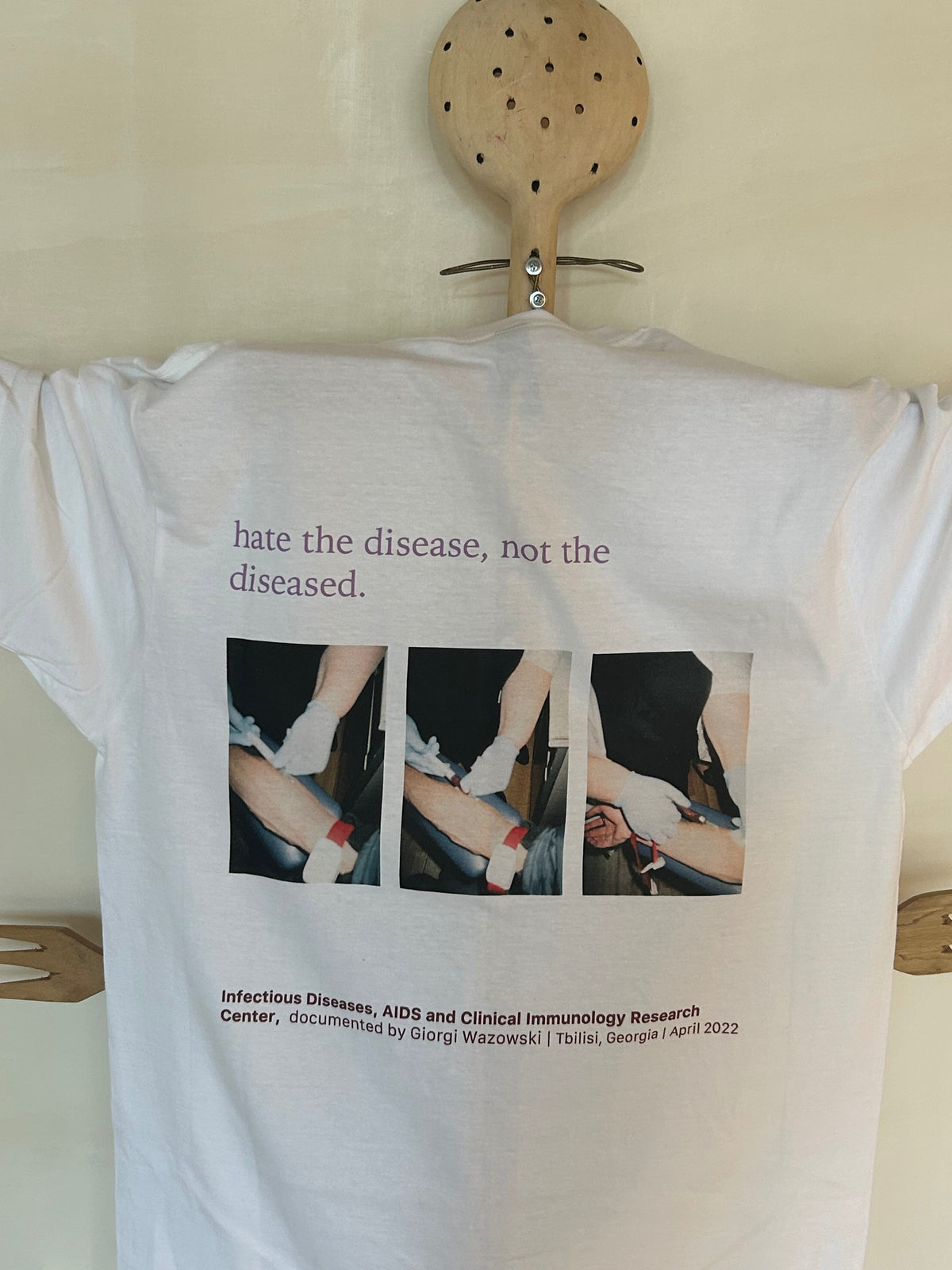 White t-shirt with printed design and text on a wooden hanger against a white background